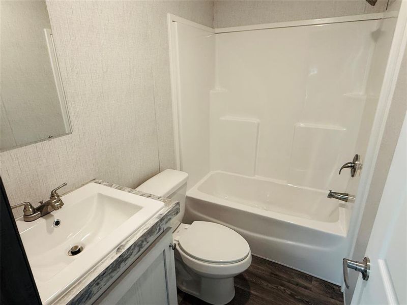 Full bathroom with vanity, dark wood-style flooring, tub / shower combination, and wallpapered walls