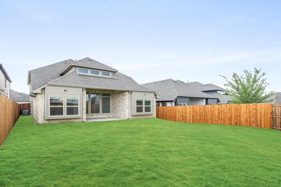 Rear view of single-story brick home with large green backyard and wood privacy fence Rear view of single-story brick home with large green backyard and wood privacy fence