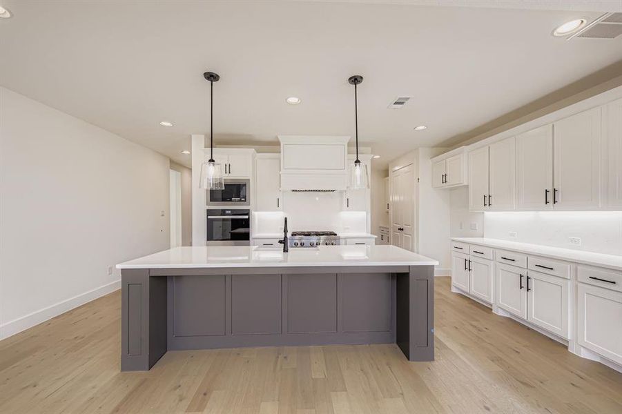 Kitchen with white cabinets, recessed lighting, an island with sink, gray cabinets, and light wood-type flooring
