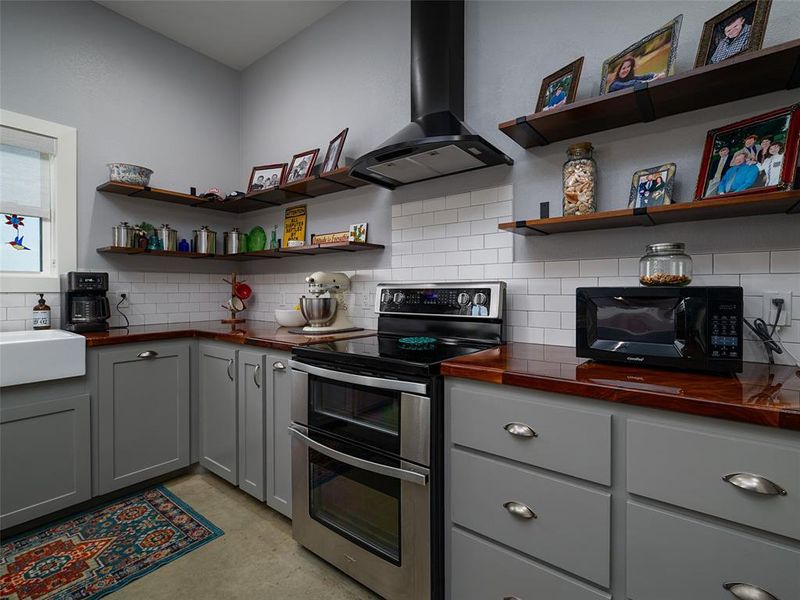 Kitchen featuring gray cabinets, range with two ovens, wall chimney range hood, and decorative backsplash Kitchen featuring gray cabinets, range with two ovens, wall chimney range hood, and decorative backsplash