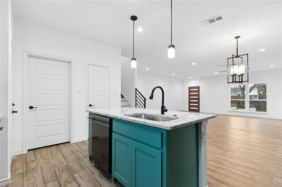 Kitchen with light hardwood / wood-style floors, sink, light stone countertops, and a center island with sink