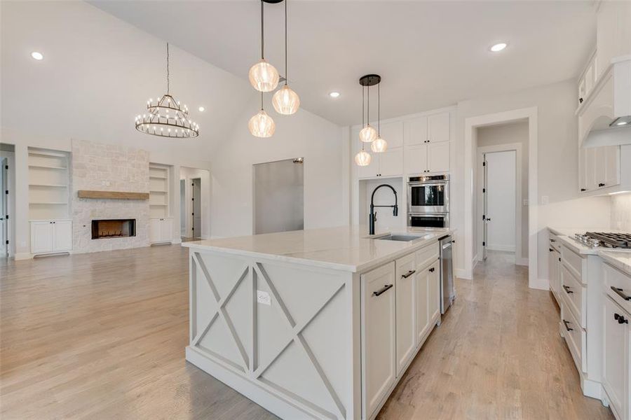 Kitchen with light hardwood / wood-style floors, white cabinetry, a center island with sink, stainless steel appliances, and a stone fireplace