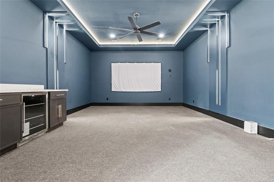 Cinema room with a raised ceiling, light colored carpet, wine cooler, and ceiling fan Cinema room with a raised ceiling, light colored carpet, wine cooler, and ceiling fan