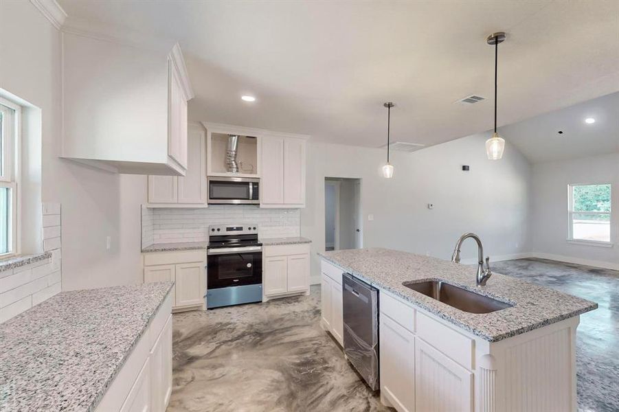 Kitchen with tasteful backsplash, stainless steel appliances, sink, white cabinets, and an island with sink