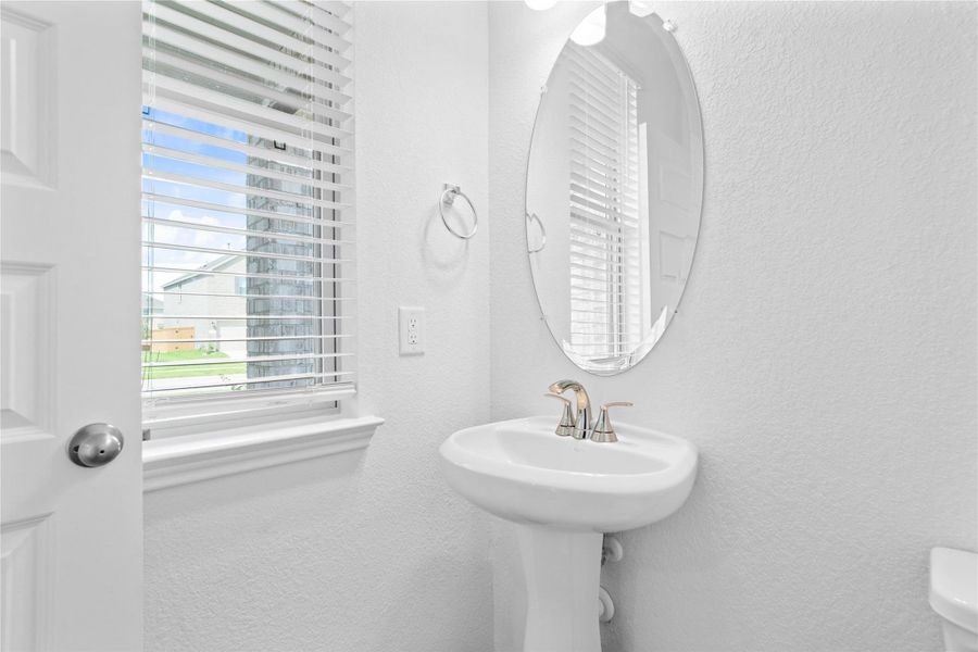 The powder room on the first floor includes a pedestal sink, mirror, window with blinds, and toilet.