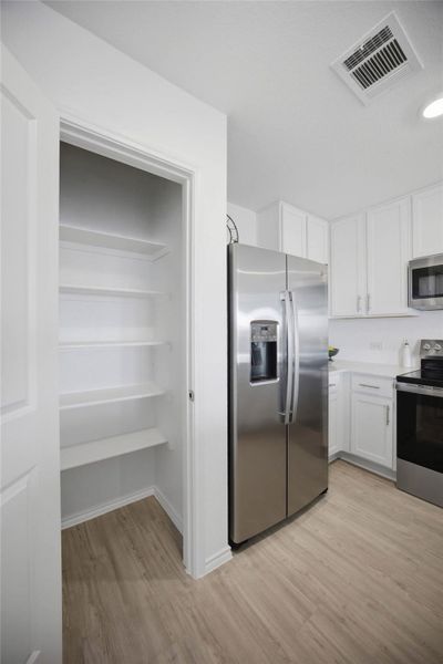 A built-in pantry with abundant shelving stands adjacent to modern kitchen cabinetry and stainless appliances.