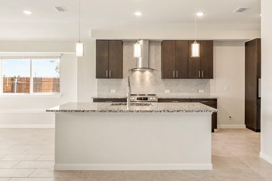 Kitchen with large granite island, dark cabinets, stainless steel range hood, and pendant lights