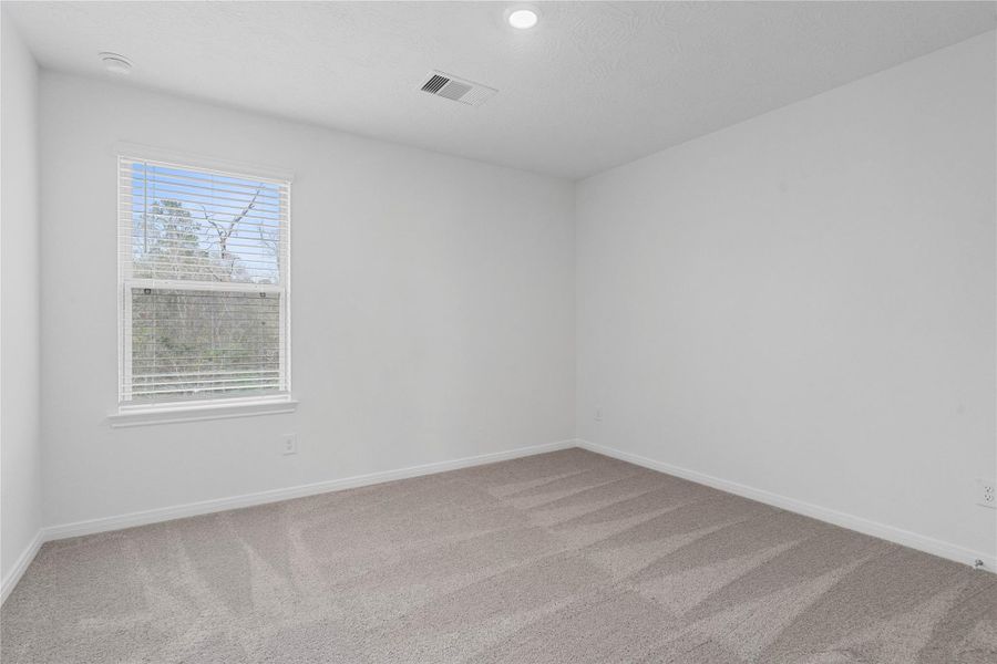 This secondary bedroom offers comfort and style with plush carpeting, neutral paint tones, recessed lighting, a large window with blinds, and a generously sized closet.