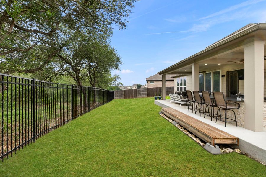 Expansive backyard featuring a manicured lawn, a black wrought iron fence, and mature trees along the property line