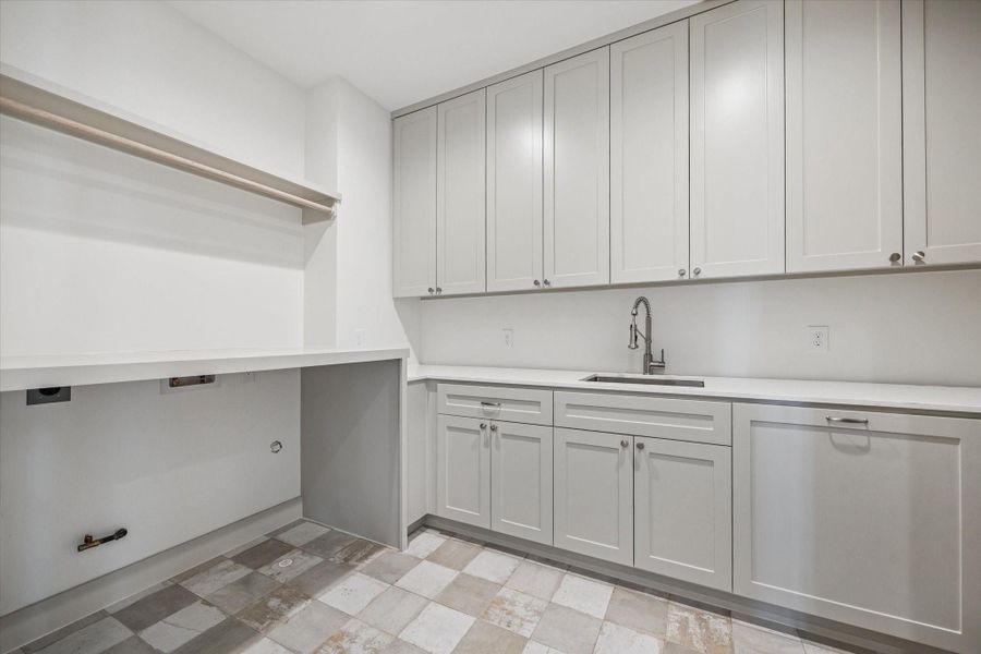 Generously sized laundry room offers full height cabinetry, expansive folding counter space, and a utility sink for added convenience. Checkerboard tile flooring introduces subtle character while keeping this hardworking space bright and polished.
