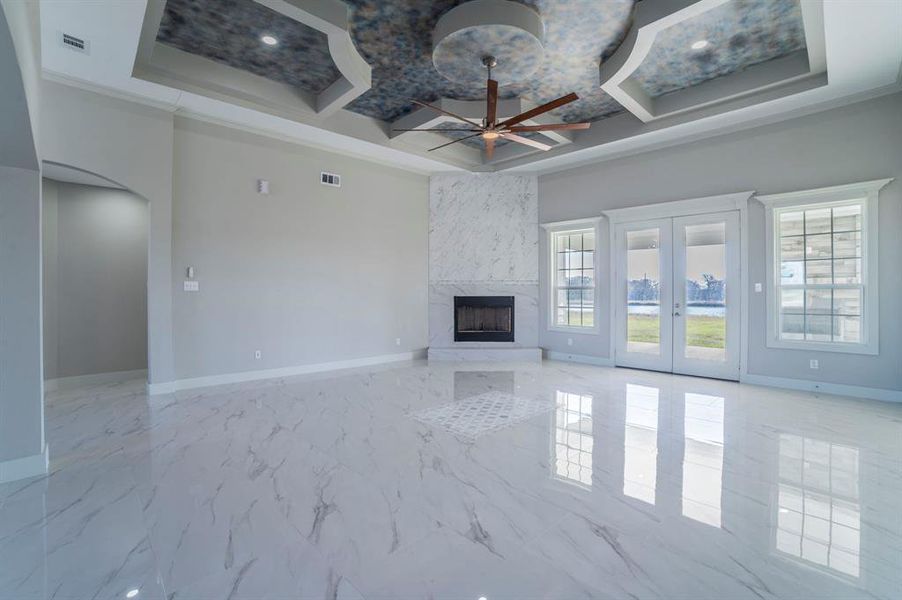 Unfurnished living room featuring light marble finish flooring, a ceiling fan, a fireplace, arched walkways, and coffered ceiling