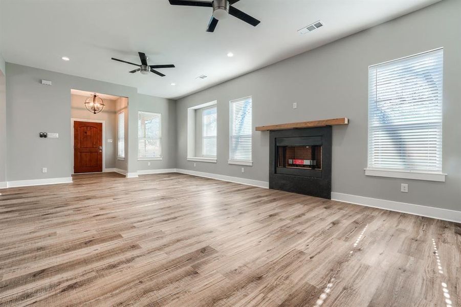 Unfurnished living room featuring ceiling fan with notable chandelier and light hardwood / wood-style floors