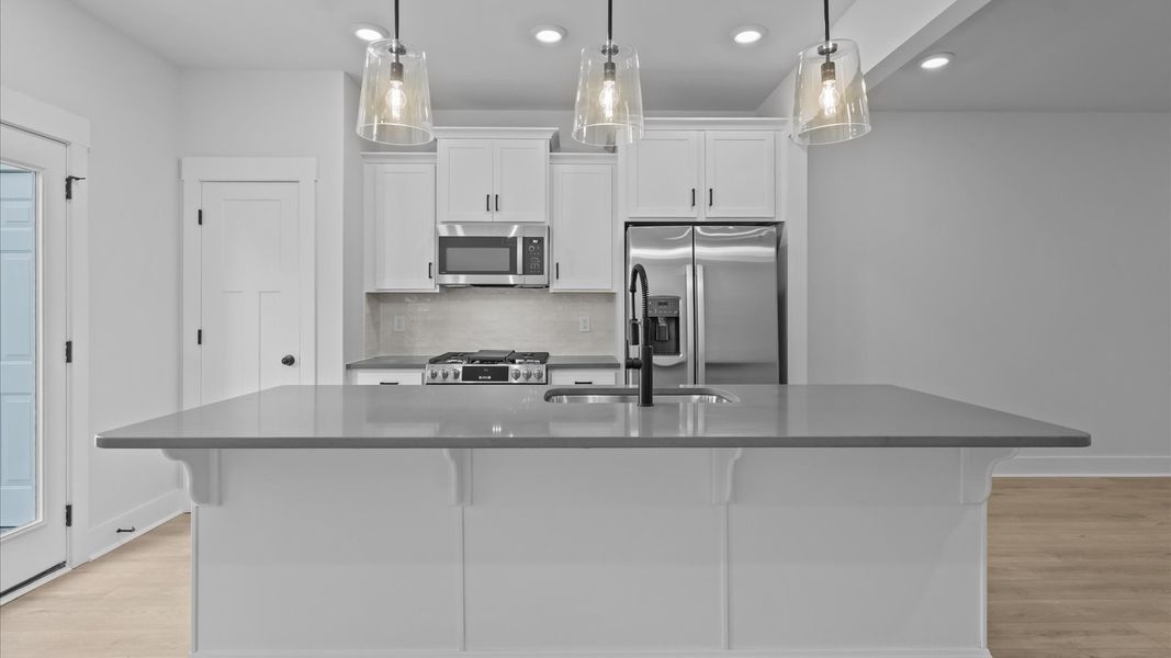 Vibrant and open kitchen centered around a 9-foot island with elegant pendant lighting above Vibrant and open kitchen centered around a 9-foot island with elegant pendant lighting above