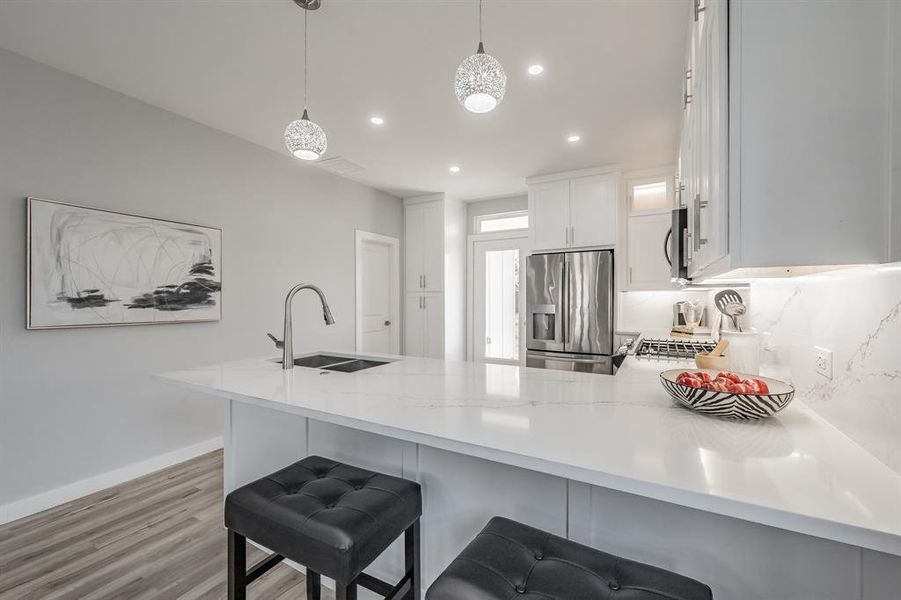 Kitchen with sink, appliances with stainless steel finishes, white cabinetry, hanging light fixtures, and kitchen peninsula