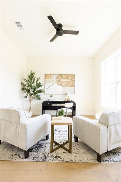 Bright room featuring light wood-finish flooring, a contemporary black ceiling fan, and ample natural light from a prominent window