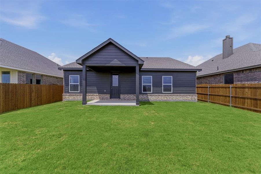 Expansive backyard featuring a covered patio, dark gray siding, light-colored stone skirting, multiple windows with white trim, and a full wood privacy fence