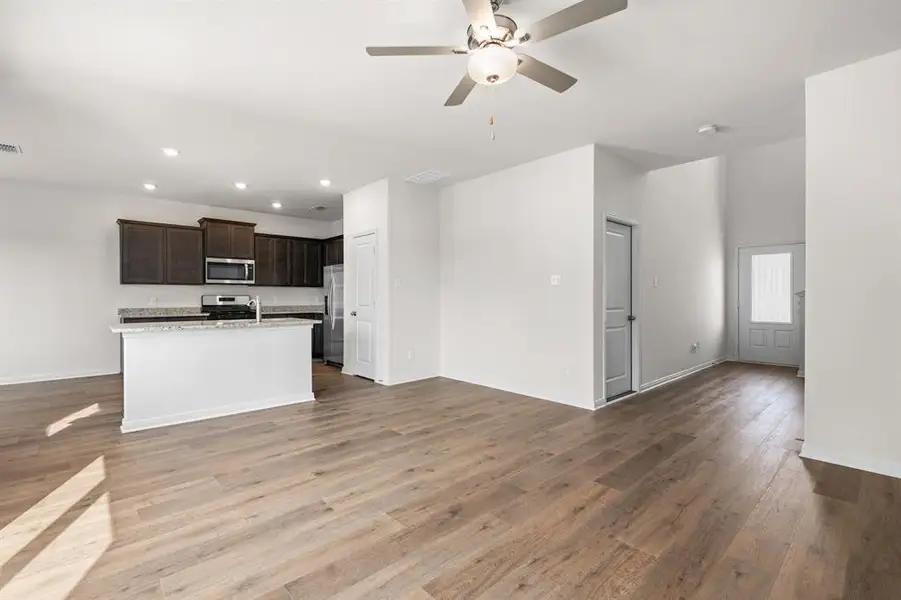 Kitchen featuring open floor plan, dark brown cabinetry, an island with sink, light wood-style flooring, and stainless steel appliances