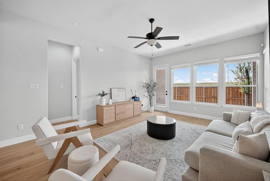 Spacious living area featuring light wood-finish flooring, a contemporary ceiling fan, and multiple windows providing ample natural light