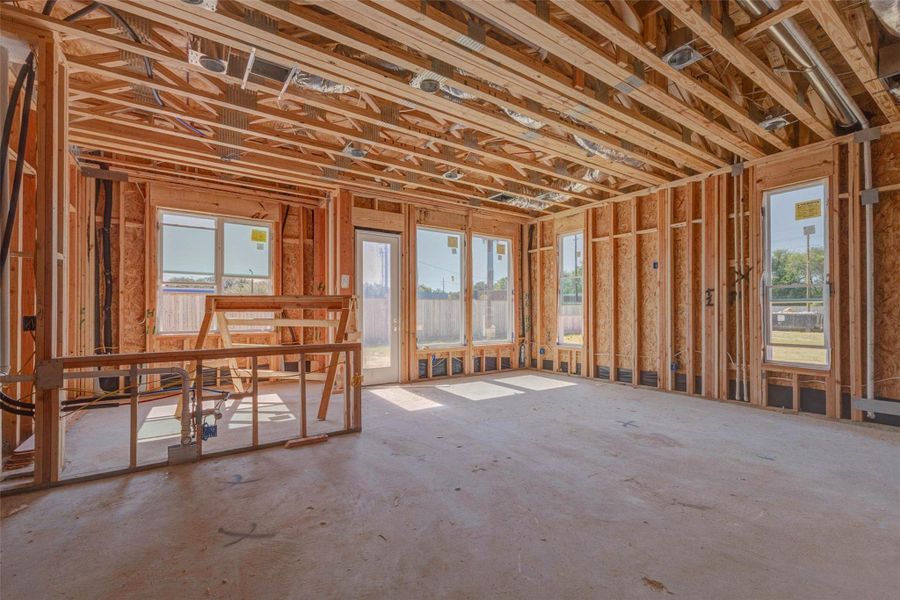 Bright open-concept living and kitchen area under construction with large windows, rear door, exposed framing, and visible mechanical systems overhead. This view captures the future heart of the home, where natural light, backyard access, and an efficient layout will come together to create a comfortable space for gathering, dining, and relaxing. Bright open-concept living and kitchen area under construction with large windows, rear door, exposed framing, and visible mechanical systems overhead. This view captures the future heart of the home, where natural light, backyard access, and an efficient layout will come together to create a comfortable space for gathering, dining, and relaxing.