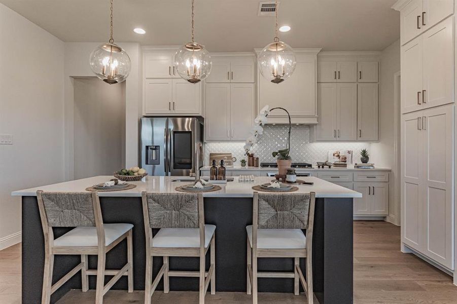 Kitchen with light hardwood / wood-style floors, an island with sink, stainless steel appliances, decorative light fixtures, and backsplash