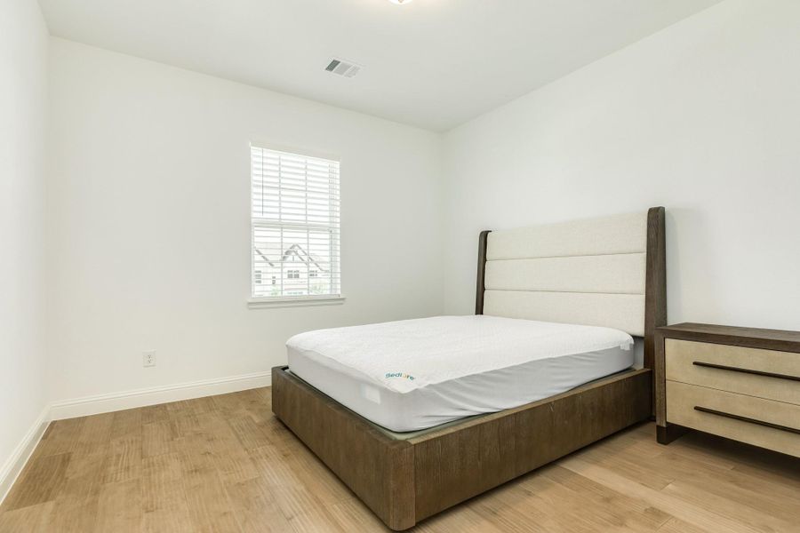 Spacious upstairs secondary bedroom featuring elegant wood floors, a large walk-in closet, and a street-facing window that provides excellent natural light.