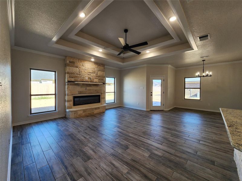 Unfurnished living room with a ceiling fan, a fireplace, ornamental molding, dark wood-type flooring, and a textured ceiling