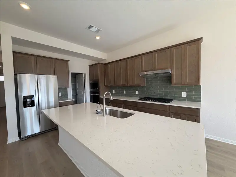 Kitchen featuring tasteful backsplash, stainless steel appliances, light stone counters, dark wood finished floors, and an island with sink