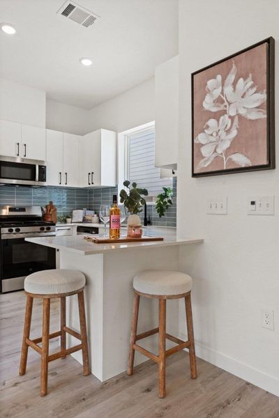 The kitchen features white cabinetry, stainless steel appliances, a tiled backsplash, and recessed lighting