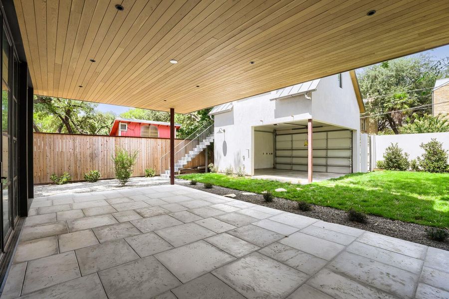 An inviting covered patio with a paved surface extends to a vibrant green lawn and detached garage.