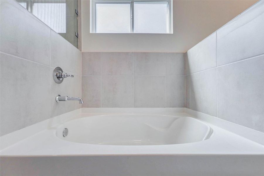 Soaking tub detail with neutral tile surround, chrome fixtures, frosted privacy window, and a clean white tub basin. This relaxing bath area offers a quiet place to unwind, with soft natural light and simple modern finishes that complement the rest of the primary suite.