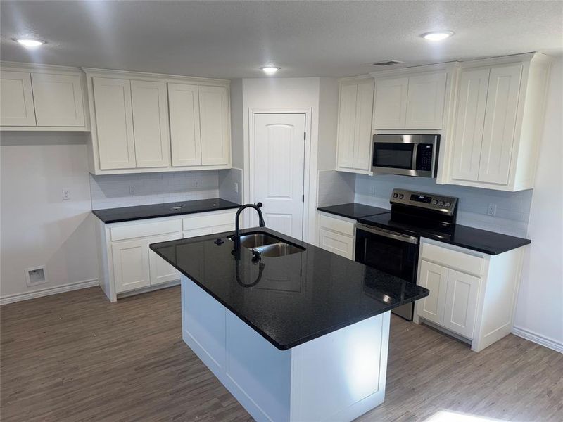 Kitchen featuring wood-type flooring, white cabinetry, sink, a center island with sink, and range with electric stovetop