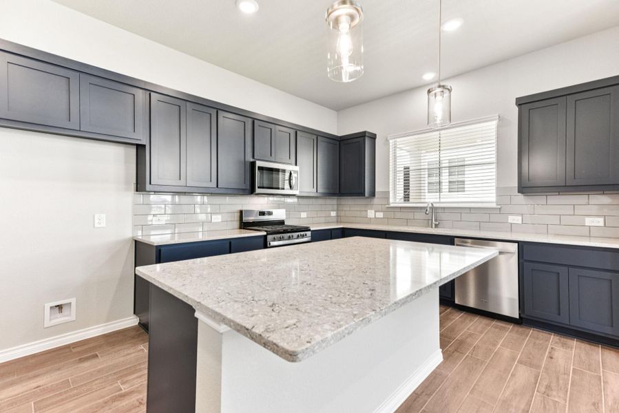 Kitchen featuring wood finish floors, light stone countertops, decorative light fixtures, stainless steel appliances, and recessed lighting Kitchen featuring wood finish floors, light stone countertops, decorative light fixtures, stainless steel appliances, and recessed lighting