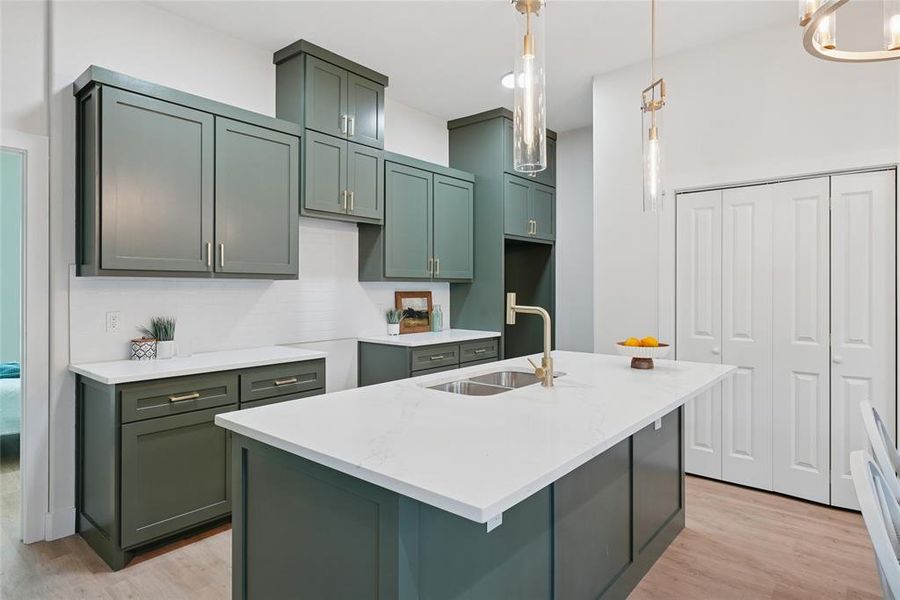 Kitchen with light stone counters, light wood-style flooring, green cabinets, and an island with sink