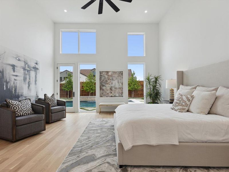 Bedroom with a towering ceiling, access to exterior, light wood-type flooring, and ceiling fan