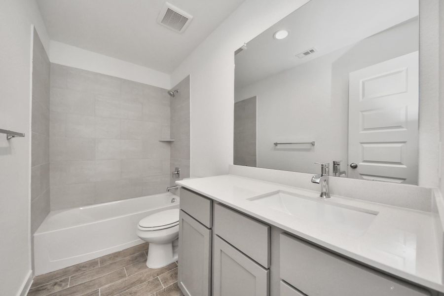 Secondary bath features tile flooring, bath/shower combo with tile surround, light stained wood cabinets, beautiful light countertop.