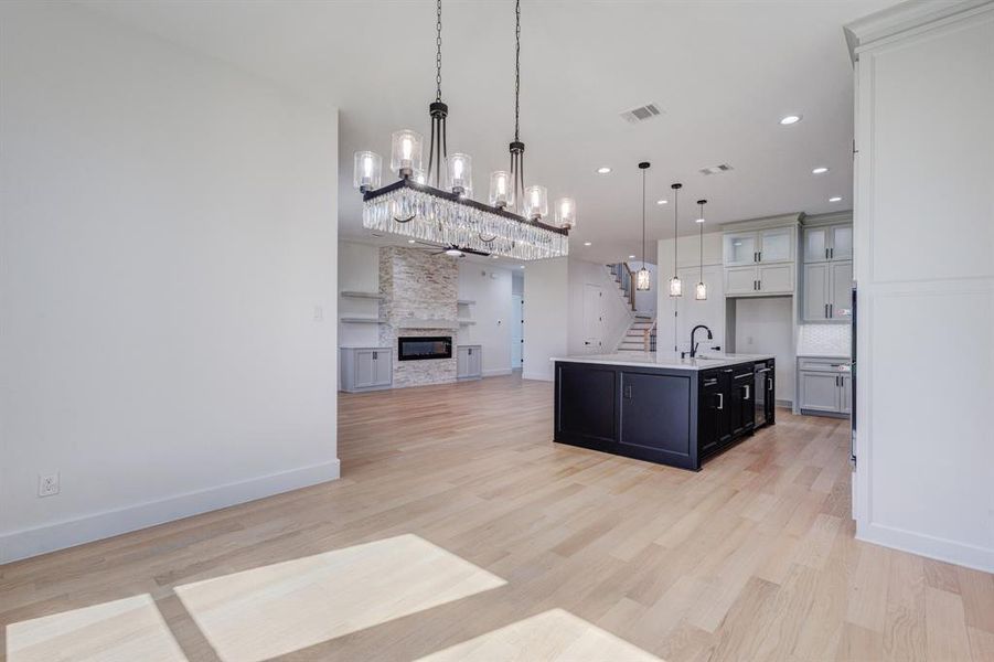 Open-concept living space with light wood-finish flooring, a contemporary linear chandelier, and recessed lighting Open-concept living space with light wood-finish flooring, a contemporary linear chandelier, and recessed lighting