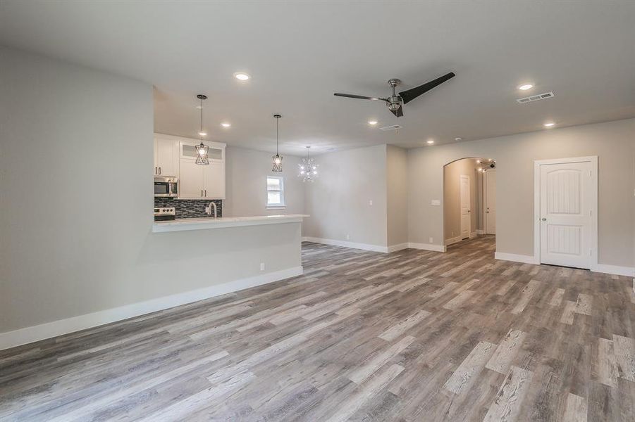 Unfurnished living room with light wood-type flooring and ceiling fan with notable chandelier