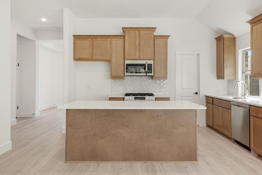 Kitchen with large center island, wood cabinets, white countertops, and stainless steel appliances on light hardwood floors