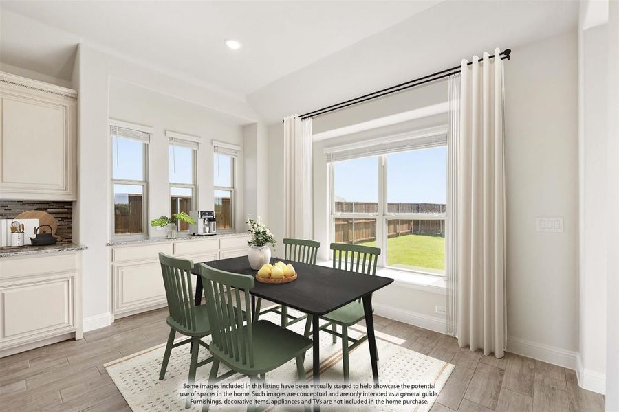 Bright dining area with dark table, green chairs, large windows, and wood-look floors adjacent to white kitchen cabinets.
