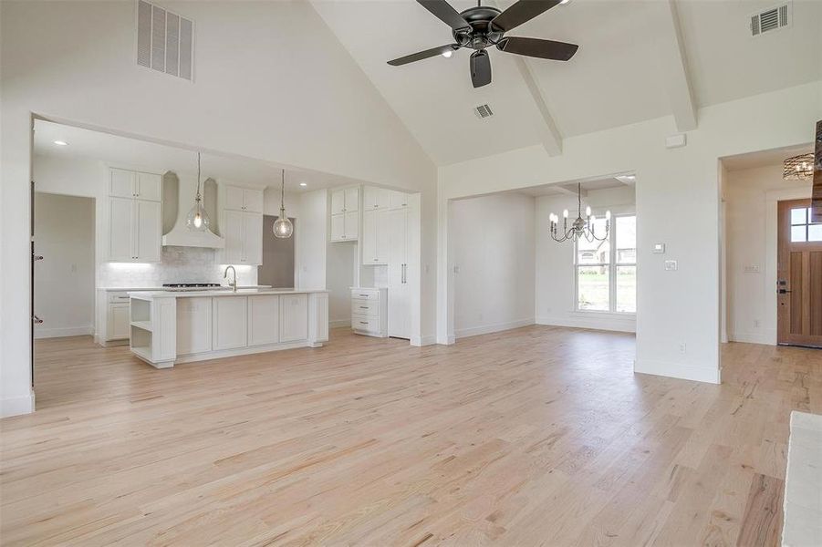 Unfurnished living room with a chandelier, high vaulted ceiling, light wood-style flooring, ceiling fan, and baseboards