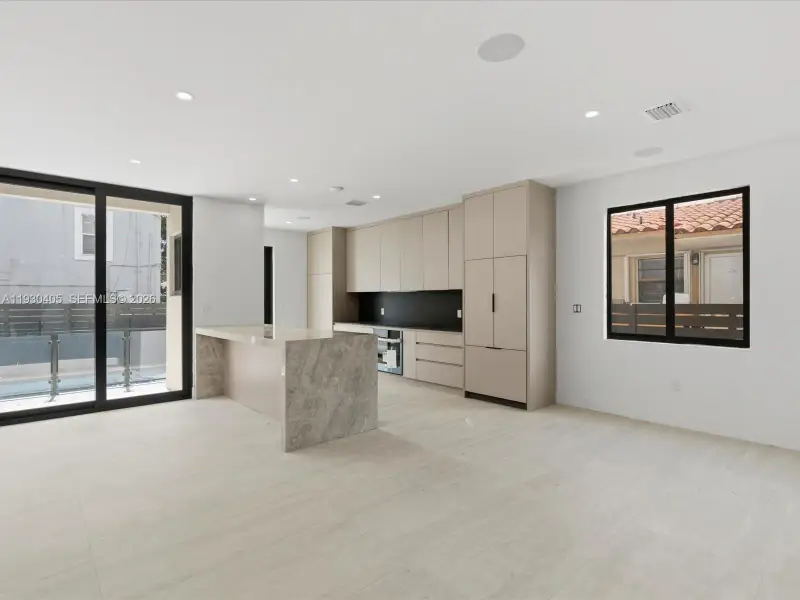 Kitchen featuring floor-to-ceiling cabinetry, a stone-finish waterfall island, matte black backsplash, integrated refrigerator, and large-format tile flooring Kitchen featuring floor-to-ceiling cabinetry, a stone-finish waterfall island, matte black backsplash, integrated refrigerator, and large-format tile flooring