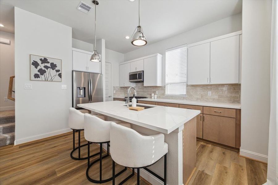 The modern kitchen showcases a clean, stylish design with light wood cabinetry, a large quartz island, and stainless steel appliances. The backsplash features a warm, textured tile that adds a touch of elegance to the bright and functional space.