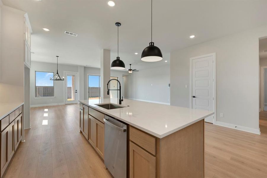 Kitchen featuring an island with sink, dishwasher, open floor plan, and light wood-style flooring