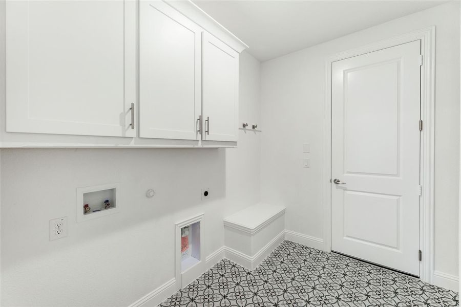 Laundry and mudroom with white cabinets, built-in bench, washer hookups, and patterned tile floor