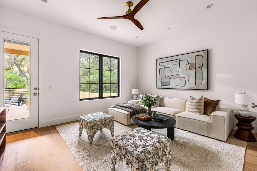 Warm hardwood floors complement a large black-framed window framing tranquil green views.