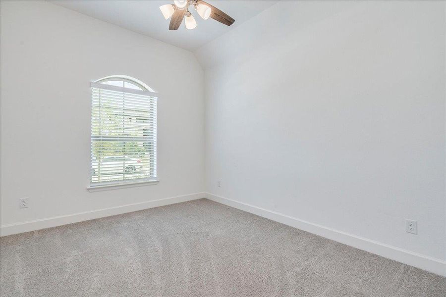 This room features a vaulted ceiling with a ceiling fan, a window with an arched top, and carpeting