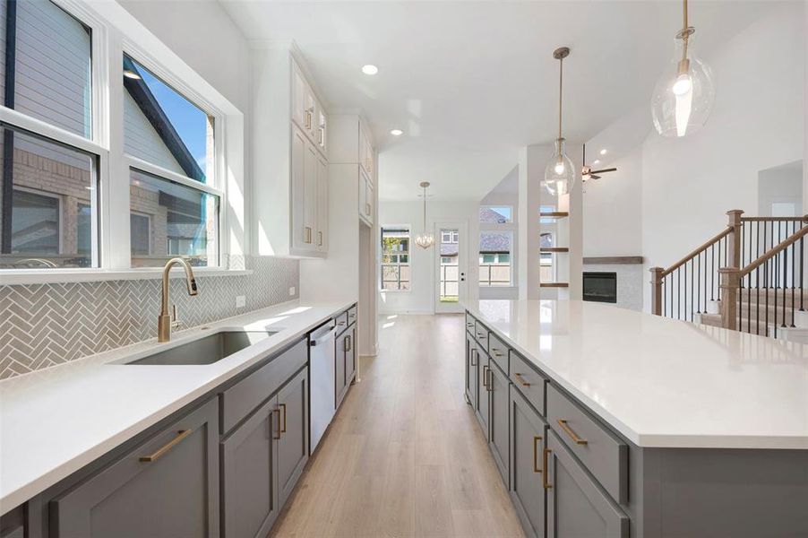 Two tone kitchen featuring decorative light fixtures, light wood-style floors, a glass covered fireplace, dual tone cabinets, and stainless steel dishwasher