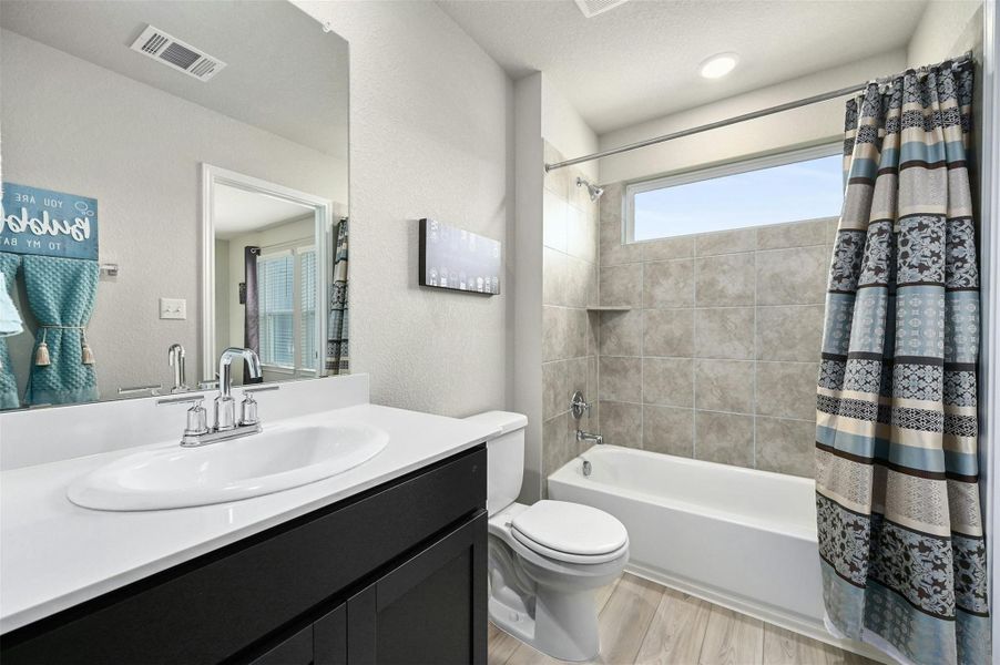 Full bathroom with a textured ceiling, toilet, vanity, and shower / tub combo with curtain