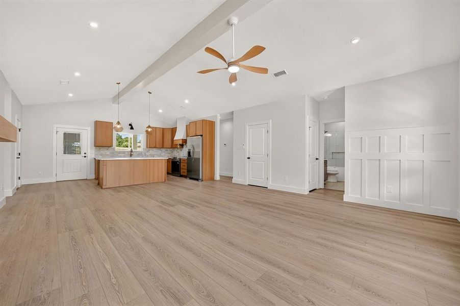 Open-concept living space featuring vaulted ceilings with exposed beam, recessed lighting, and wood-finish flooring