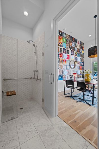 Walk-in shower featuring a glass enclosure, white patterned wall tiles, a built-in wooden seat, and a rainfall showerhead